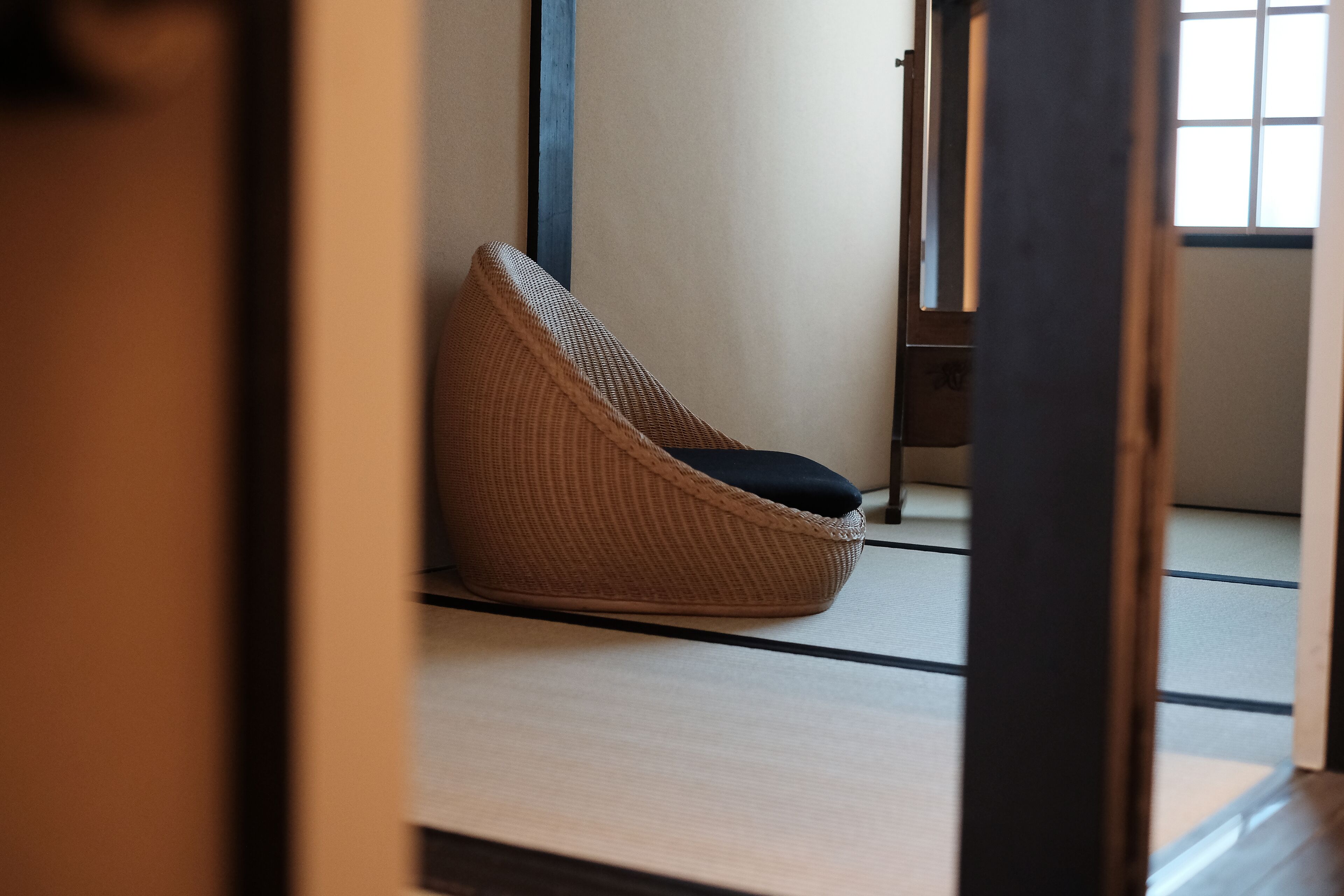 A tatami mat room with a woven chair and a wooden door.