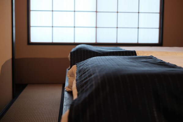 Een kamer met een bed, een raam met een rasterpatroon en een tatami mat.