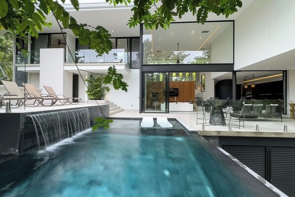 A modern house with a swimming pool, outdoor seating, and a waterfall feature.