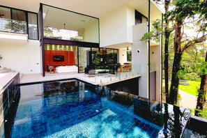 A modern house with a swimming pool, a dining area, and a large glass window overlooking the garden.