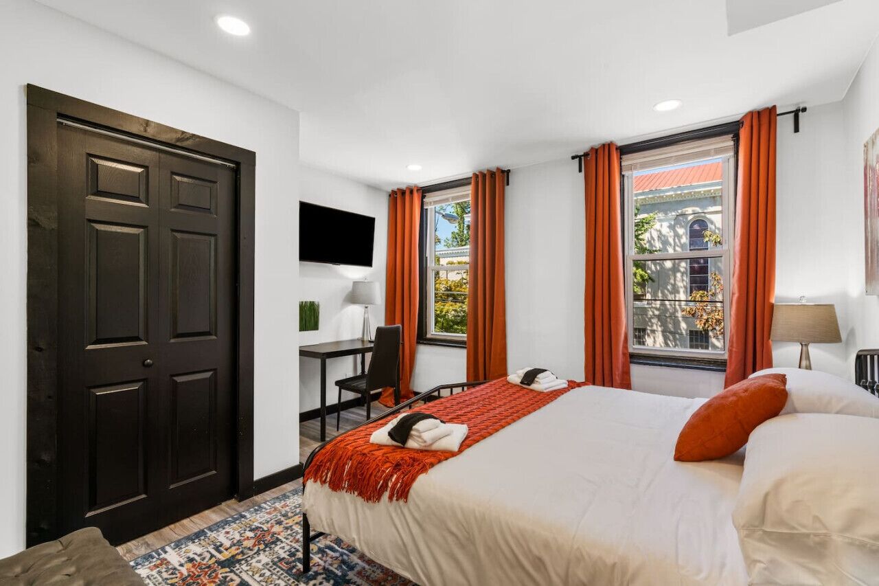 Une chambre d’hôtel avec un grand lit, un bureau, une chaise, une télévision et une fenêtre avec des rideaux.