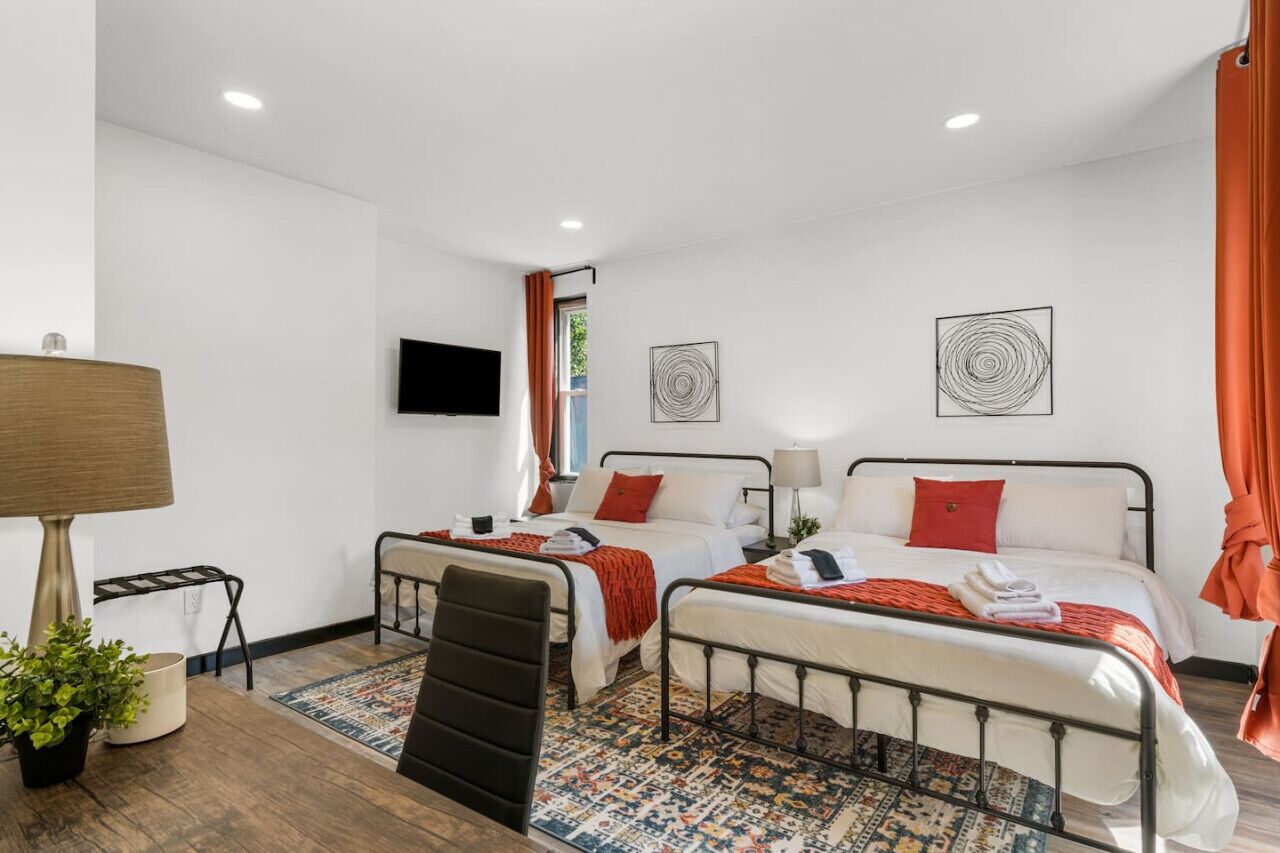 A hotel room with two beds, a desk, a chair, a TV, and artwork on the walls.