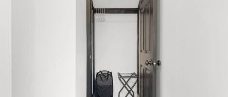 A narrow hallway with a wooden floor, a black door, and a laundry basket near the door.