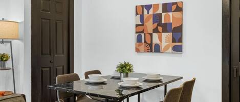 A dining area with a marble table, four chairs, and a modern abstract painting on the wall.