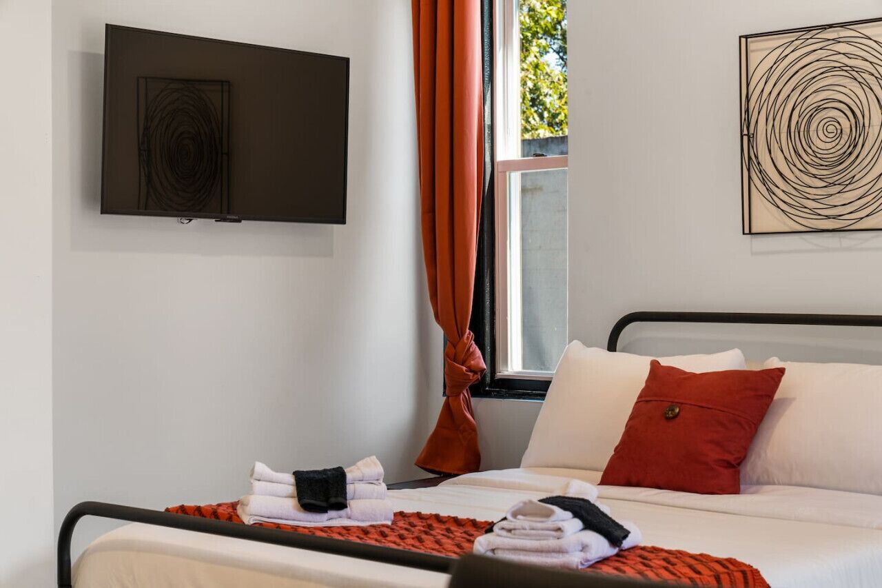 Quarto de hotel com cama, televisão de tela plana fixada na parede e janela com cortinas.
