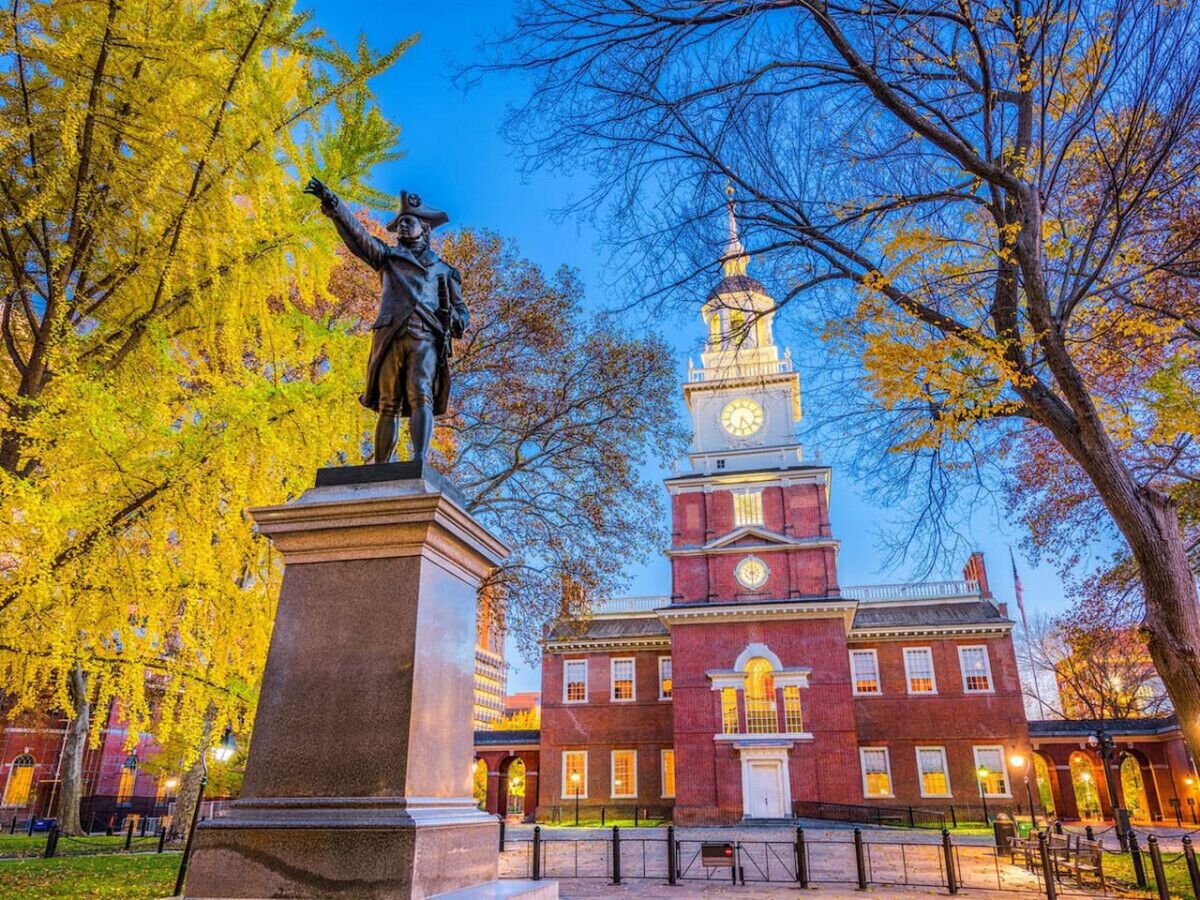A statue in a park with a red brick building in the background.
