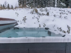 A hot tub in a snowy outdoor setting with a wooden deck and a backdrop of snow-covered trees. - Villa minnesota by Interhome (Kuhmoinen)