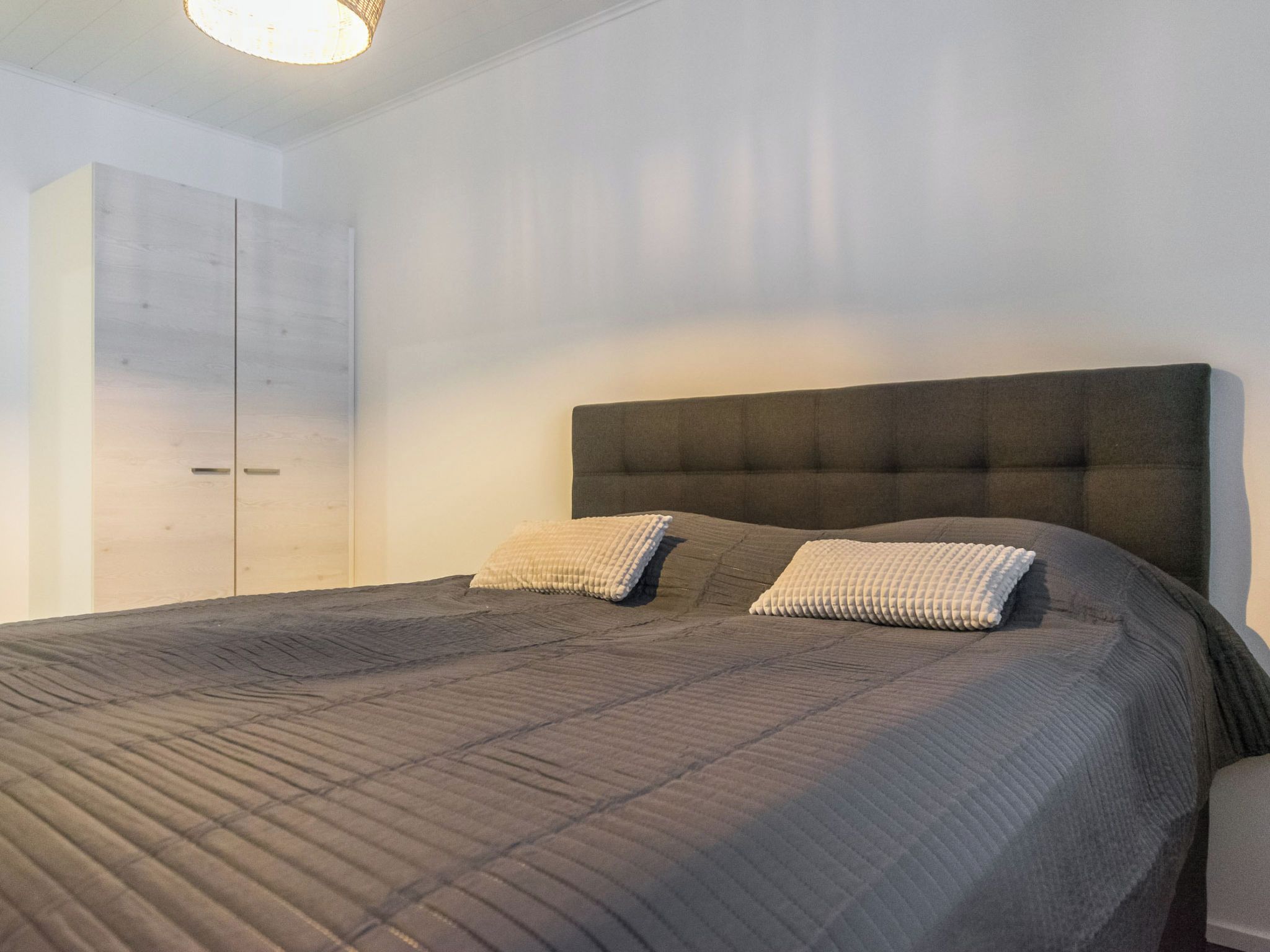 A bedroom with a large bed, two pillows, a wardrobe, and a ceiling light.