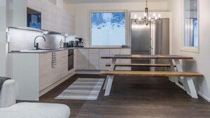 Una cocina moderna con horno empotrado, un fregadero y una cafetera. Hay una mesa de comedor con bancos y una araña colgante.