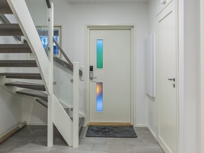 Un intérieur moderne avec un escalier blanc, une porte dotée d’un panneau en verre dépoli et un paillasson gris à l’entrée.