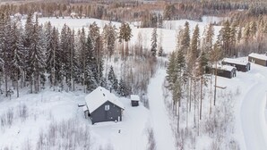 Una cabaña aislada rodeada de árboles nevados y un cielo despejado.