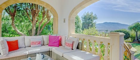 A covered outdoor seating area with wicker furniture and a view of the landscape.