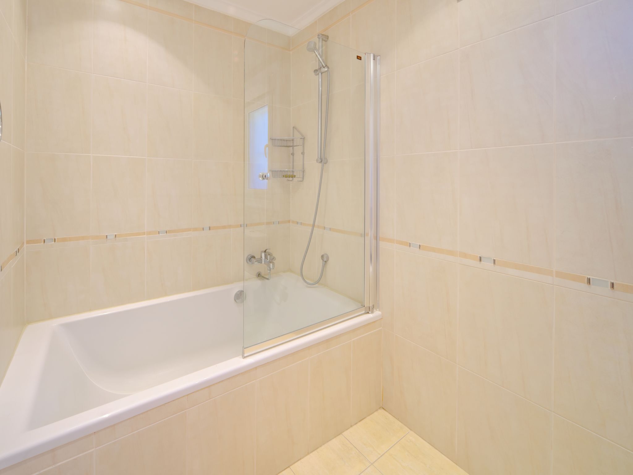 A modern bathroom with a glass-enclosed shower, a white bathtub, and beige tiled walls.