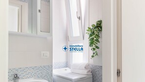 Ett badrum med handfat, tvättmaskin, spegel och ett fönster.