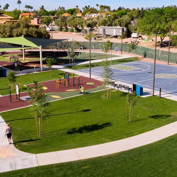 A well-maintained park with a basketball court, playground equipment, and a walking path.