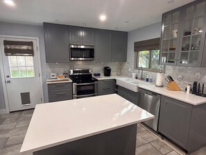A modern kitchen with grey cabinets, stainless steel appliances, and a white countertop.