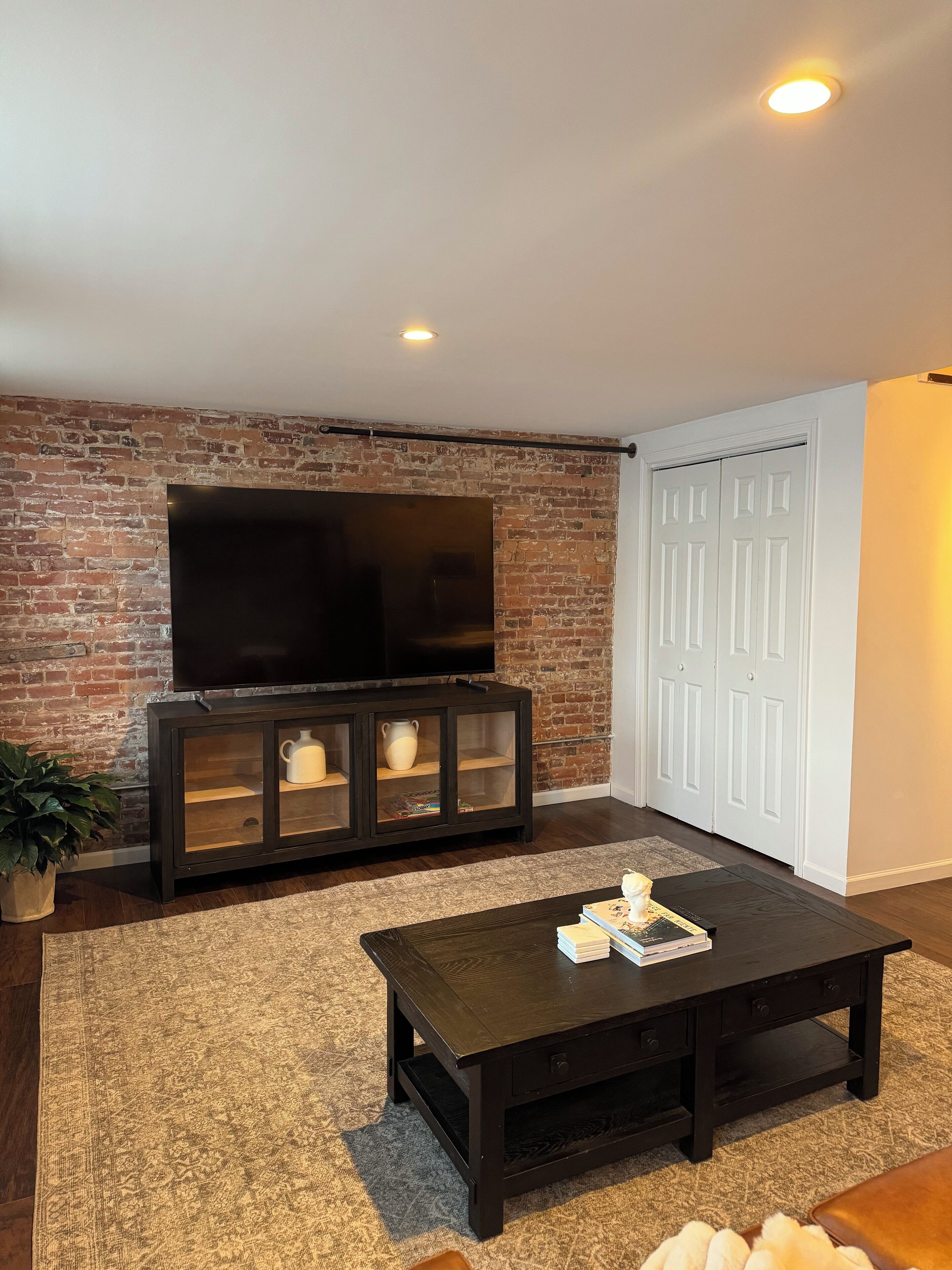 Een woonkamer met een bakstenen muur, een flatscreen televisie, een donker houten salontafel en een witte deur.