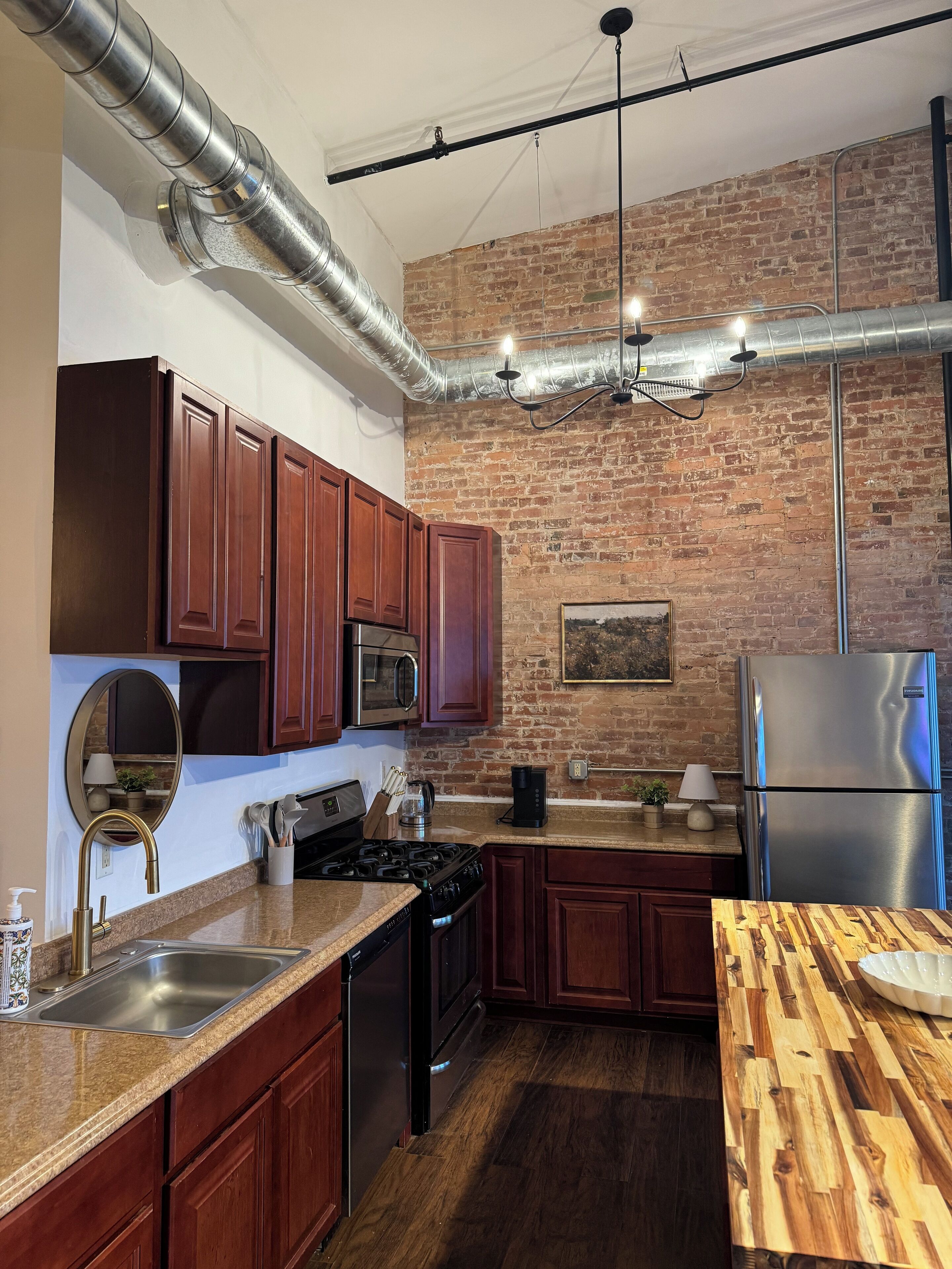 Una cocina con armarios de madera, electrodomésticos de acero inoxidable y pared de ladrillo.