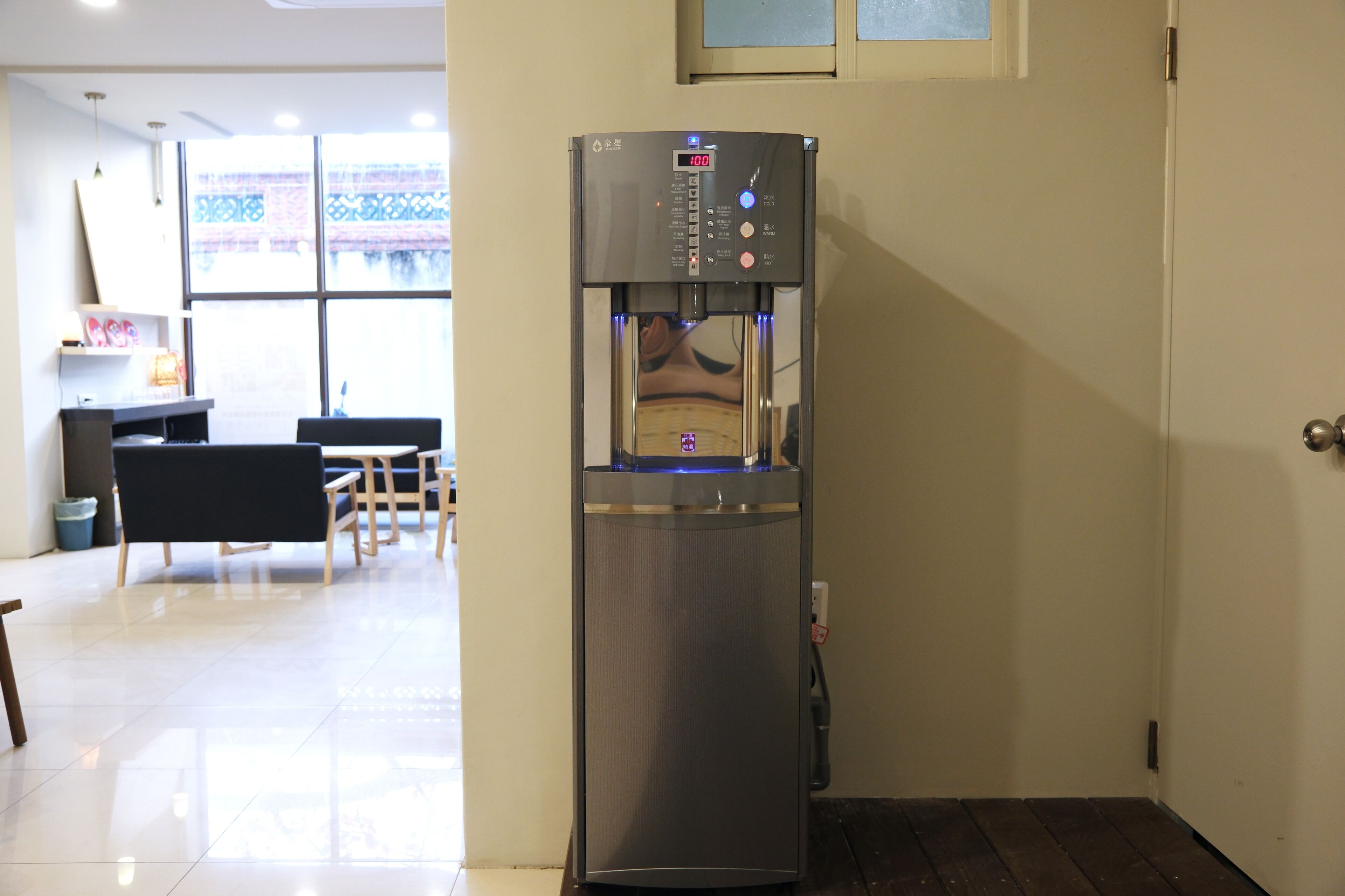 A water dispenser in a room with a tiled floor, a wooden table, and chairs.
