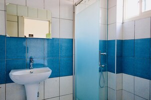 Un baño con un lavamanos blanco, un espejo encima y una cabina de ducha de vidrio.