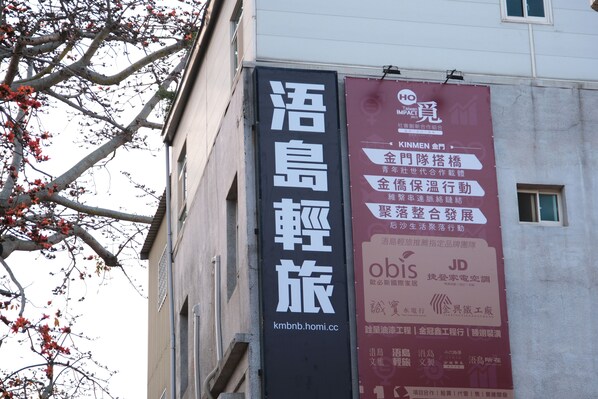 Un edificio con dos pancartas verticales. Una pancarta es negra con caracteres chinos blancos y una dirección web. La otra es roja con caracteres chinos blancos y logotipos.