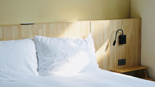 A neatly made bed with white linens in a room with wooden headboard and a small wooden nightstand.