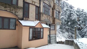 A building with a small attached structure, large windows, and a snow-covered tree. - Hotel Amar Palace (Shimla)