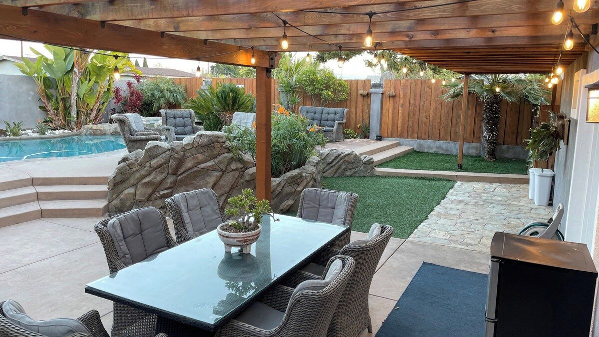 A covered outdoor patio with a table and chairs, a pool, and a small lawn area.