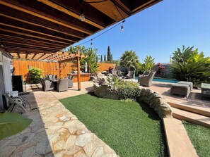 Un patio exterior con piscina, mobiliario y una pérgola.