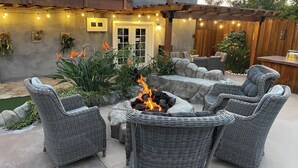 A patio with wicker furniture, a fire pit, and string lights. - 5BR Retreat w/ Salt Water Pool, Spa, Fire Pit &BBQ (San Diego)