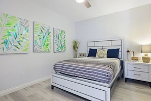 A bedroom with a bed, nightstand, wall art, and a ceiling fan.