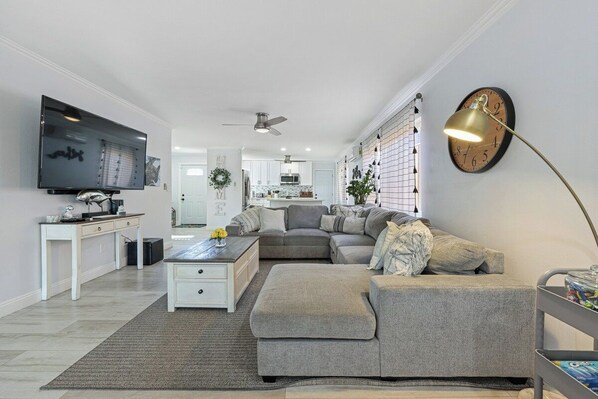A modern living room with a flat-screen TV, a sofa, a coffee table, and a desk with a lamp.