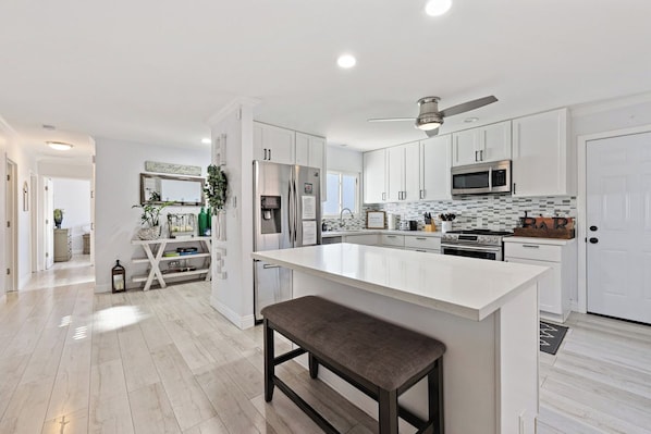 A modern kitchen with white cabinetry, a central island, and a ceiling fan.