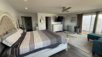 Un dormitorio moderno con una cama grande, televisión, balcón con vistas y ventilador de techo.
