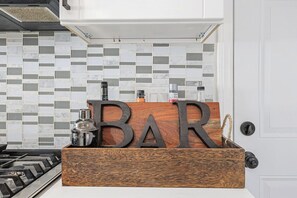 A kitchen with a tiled backsplash, a wooden bar sign, and a gas stove.