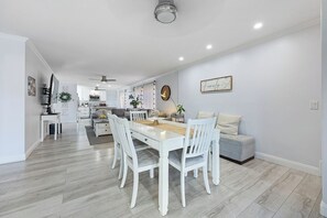 Una cocina moderna con armarios blancos, una mesa de comedor con sillas y una sala de estar con un sofá y una mesa baja.
