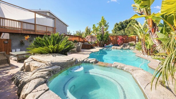 A backyard with a swimming pool, a wooden deck, and tropical plants. - 5BR Retreat w/ Salt Water Pool, Spa, Fire Pit &BBQ (San Diego)