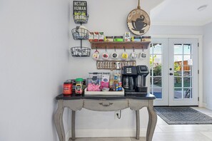 A coffee station with a coffee maker, various coffee pods, and a sign that reads 'COFFEE, ANYONE?'