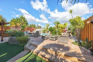 A backyard with a patio, outdoor furniture, a pool, and various plants.