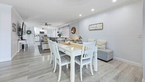 A spacious living area with a dining table, white chairs, and a grey sofa. - 5BR Retreat w/ Salt Water Pool, Spa, Fire Pit &BBQ (San Diego)