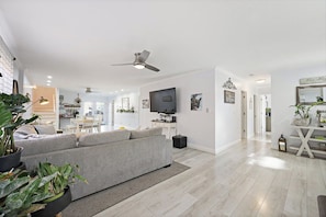 A modern living room with a grey sofa, a flat-screen TV, and a ceiling fan.
