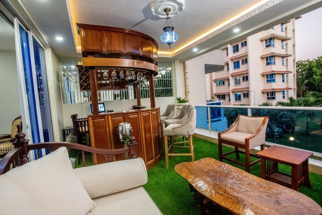 Una sala de estar con sofá, sillas, una mesa de centro de madera, una zona de bar con vasos y vistas a un edificio residencial.