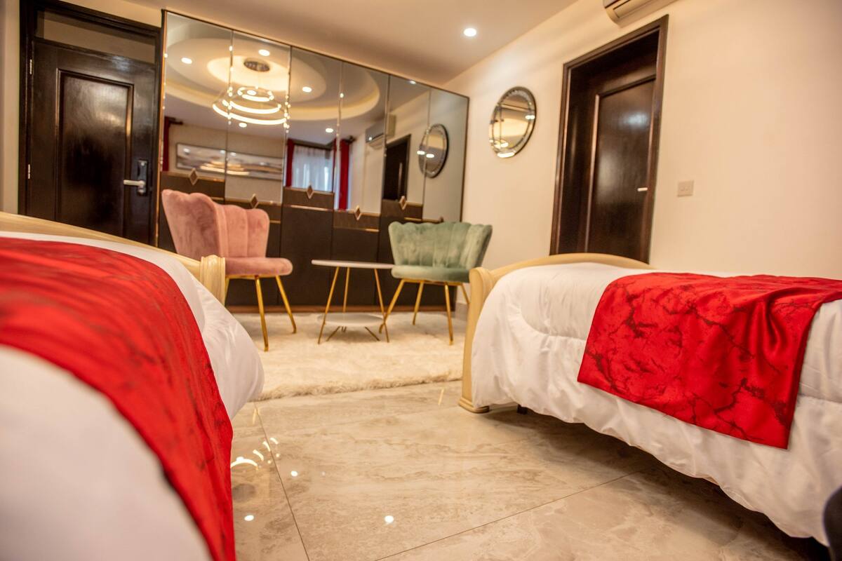 Une chambre d’hôtel avec deux lits, un grand miroir, une chaise verte et une petite table.