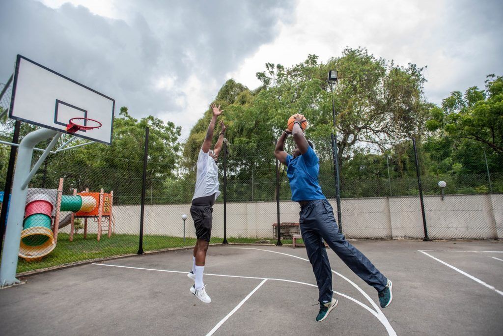Una cancha de baloncesto al aire libre con aro, valla y árboles de fondo.