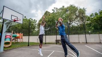 Una cancha de baloncesto al aire libre con aro, valla y árboles de fondo.