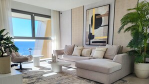 Ett modernt vardagsrum med en beige soffa, ett soffbord och en stor krukväxt.