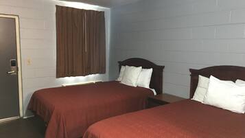 A room with two beds, a window with brown curtains, and a white brick wall.