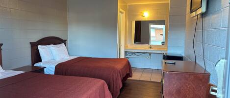 A hotel room with two beds, a desk, a chair, a mirror, and a television.