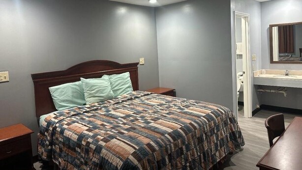 A bedroom with a bed, nightstands, a wooden headboard, a bathroom with a sink and mirror, and a dining area with a table and chairs. - Sky Inn Hotel (Birmingham)