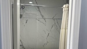 A bathroom with a shower, marble walls, and a toilet. - Sky Inn Hotel (Birmingham)